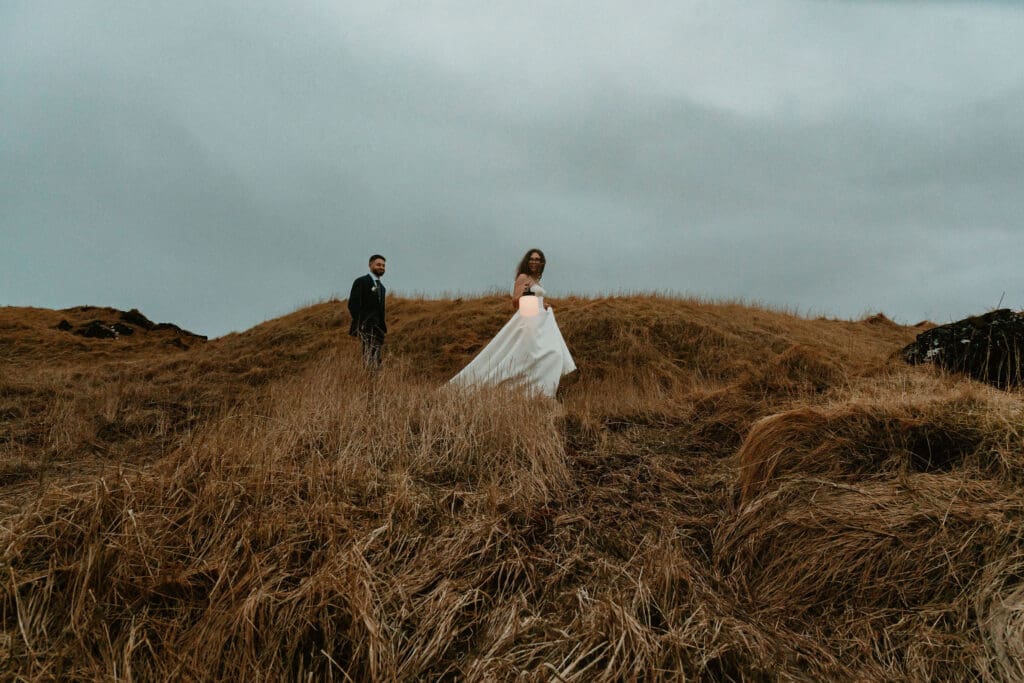 Cinematic image of an elopement couple walking through sand dunes at dusk near Búðir black church, the bride holding a lantern