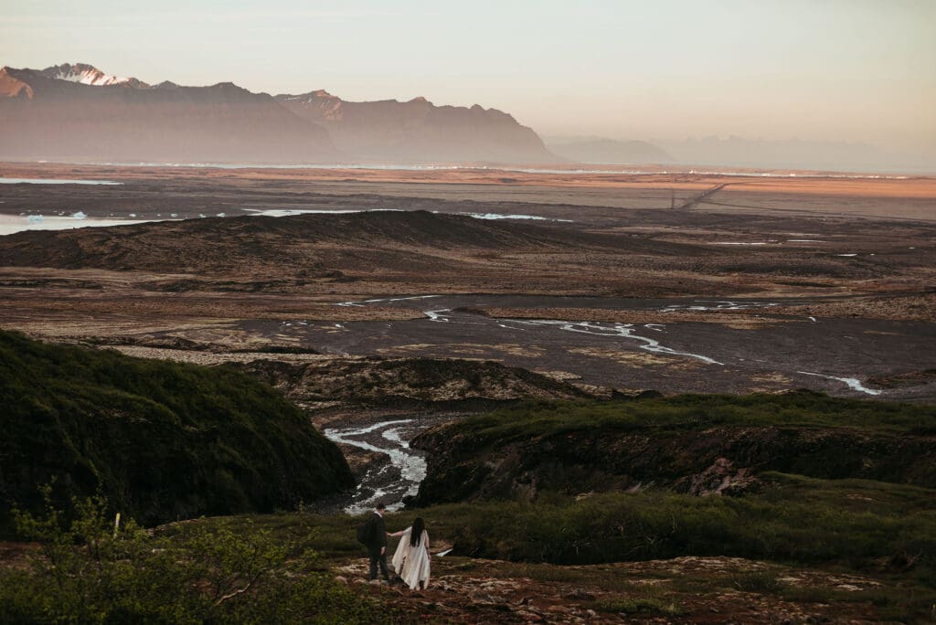 Elopement couple playfully holding hands, and hiking through a landscape of mountains, glacial, rivers, and glaciers in South East Iceland
