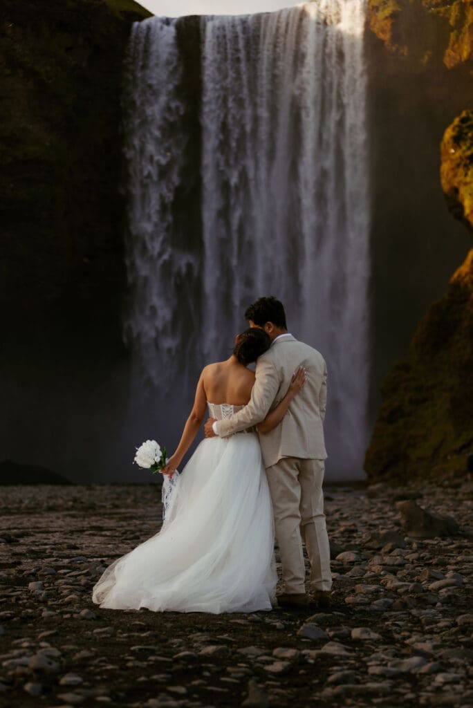 Elopement couple hugging from behind, and a cinematic Skógafoss in the background