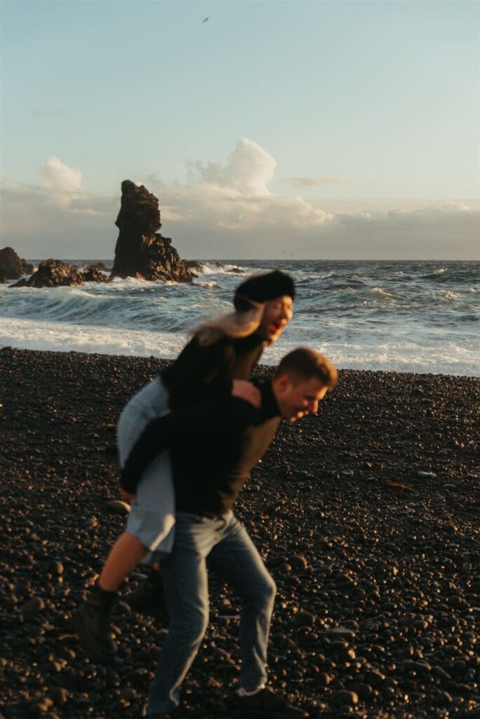 Playful couple running along the black sand at Djúpalónssandur Beach during their Iceland elopement on the Snæfellsnes Peninsula.