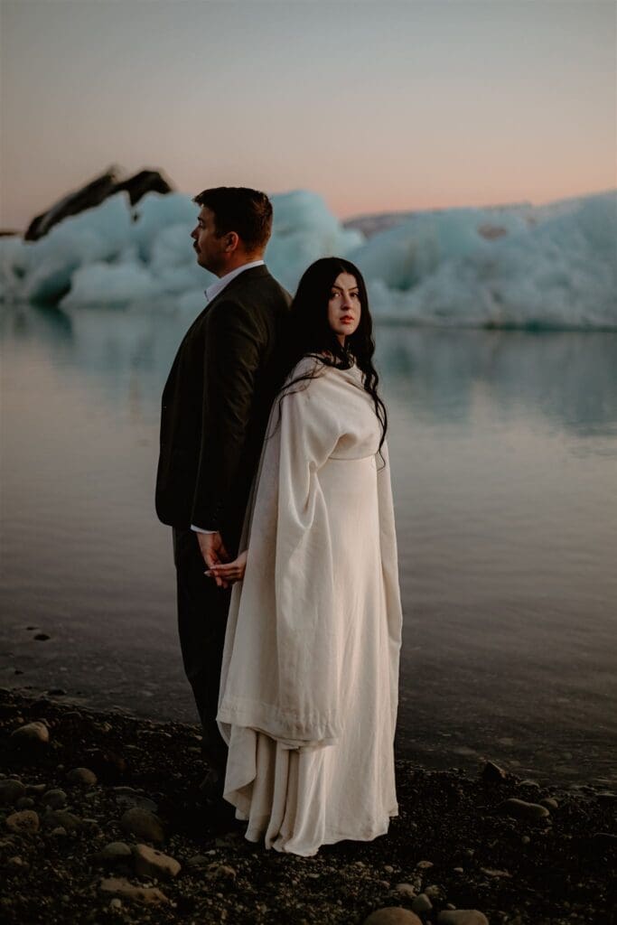 Couple holding hands at Jökulsárlón Glacier Lagoon during an Iceland elopement, with floating icebergs and soft sunset tones.
