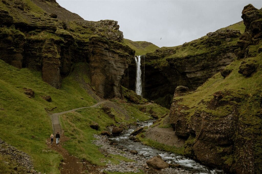 Couple standing near Kvernufoss waterfall during their Iceland elopement, surrounded by mossy cliffs and flowing water.
