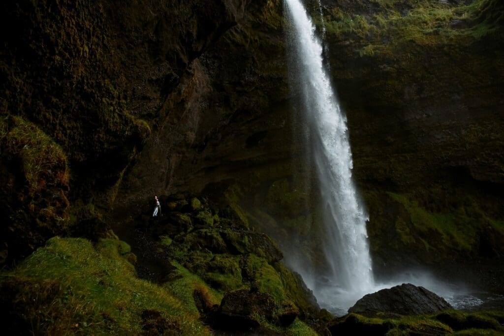 Wide view of Kvernufoss waterfall during an Iceland elopement, capturing the scale of the falls and the couple below.
