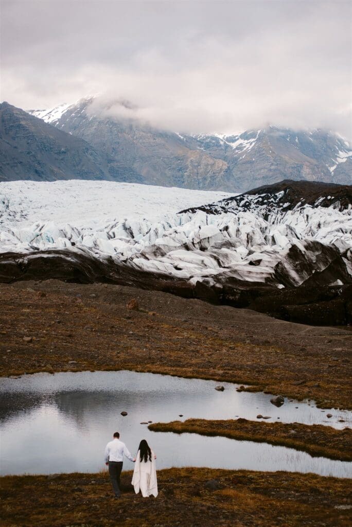 Couple walking hand in hand near a glacier lake in Skaftafell National Park, Iceland during a scenic elopement.