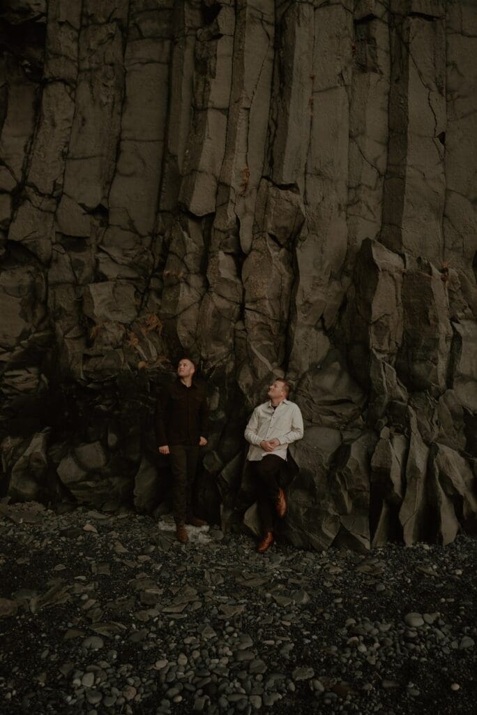 A gay couple standing under the basalt columns at reynisfjara black sand beach