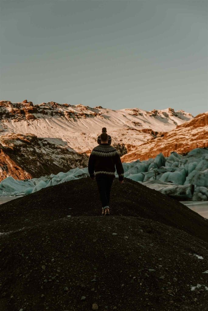 Male engagement photos in Iceland in December, black sands contrasting icy blue glacier and fiery red mountains from sunlight