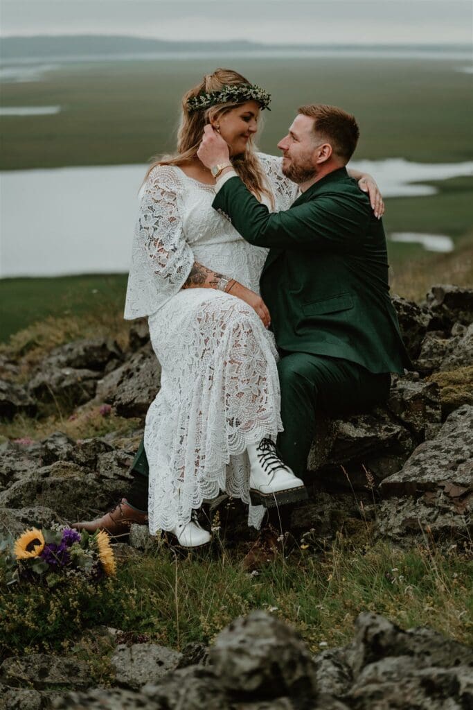 Couple sitting together on rocky hills overlooking open landscape during their Iceland elopement, sharing a quiet, joyful moment.