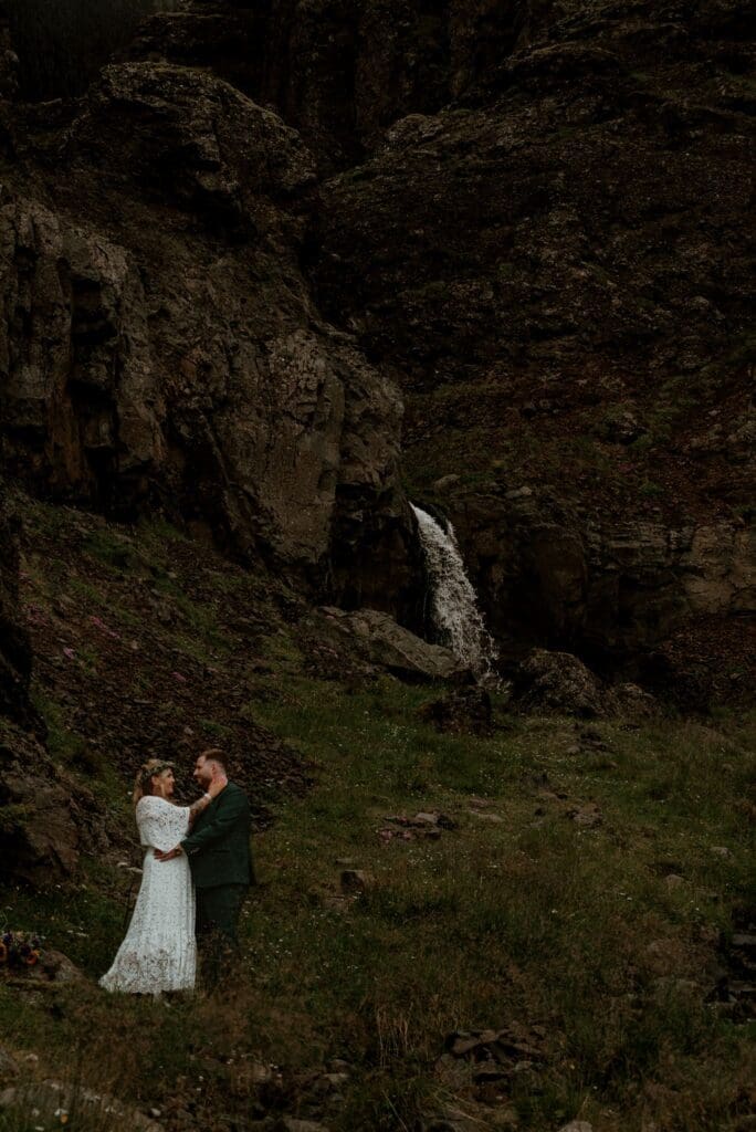 Eloping couple standing beneath a small waterfall in the Icelandic highlands, sharing an intimate moment during their adventure elopement.