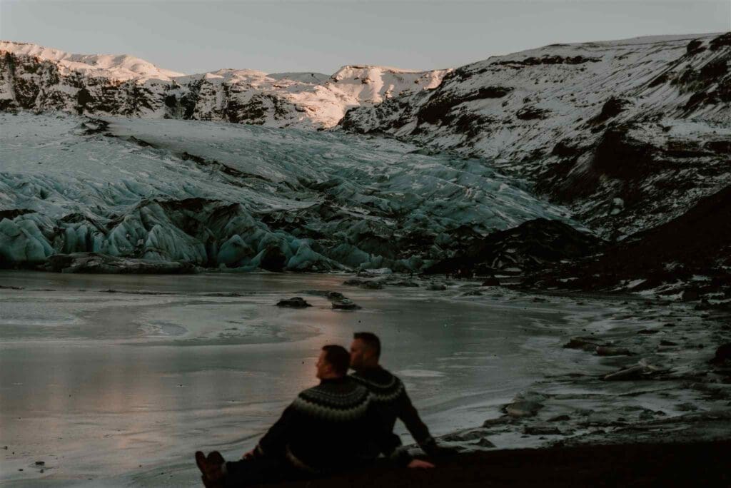 Close-up photo of a couple sitting overlooking a glacier lagoon in winter