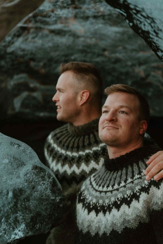 Two men wearing Icelandic sweaters, posing in an ice cave for their engagement photos