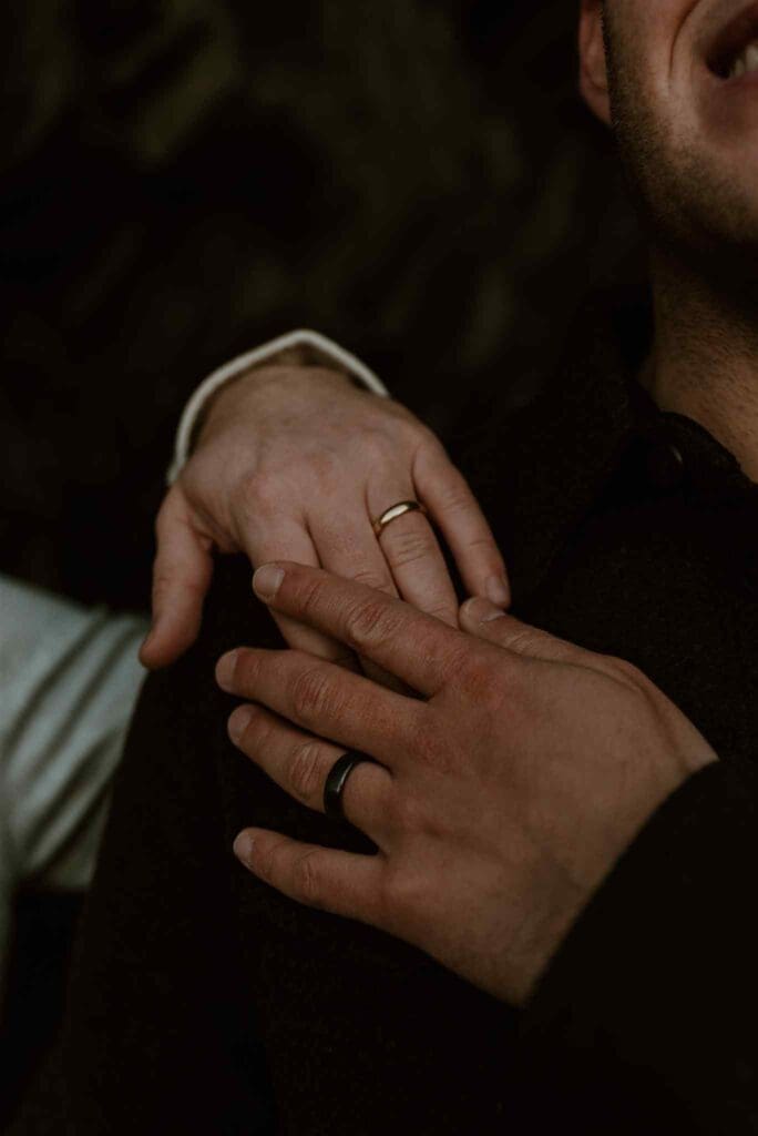 Two men's hands embracing, showcasing their engagement rings