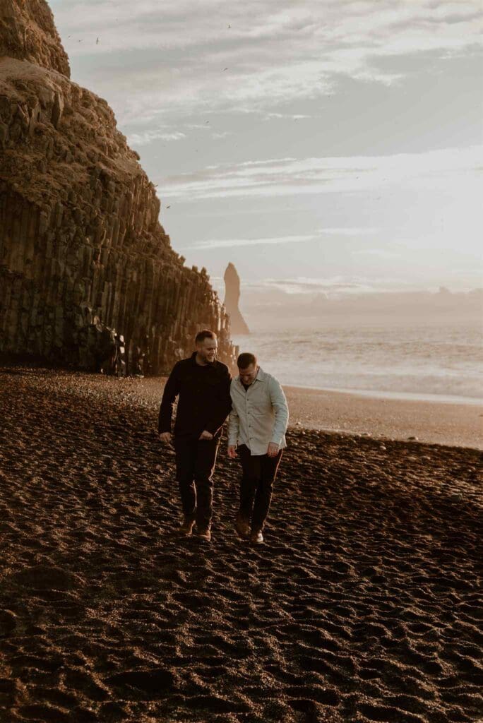 Couple lovingly walks on black sand beach in Iceland during golden hour