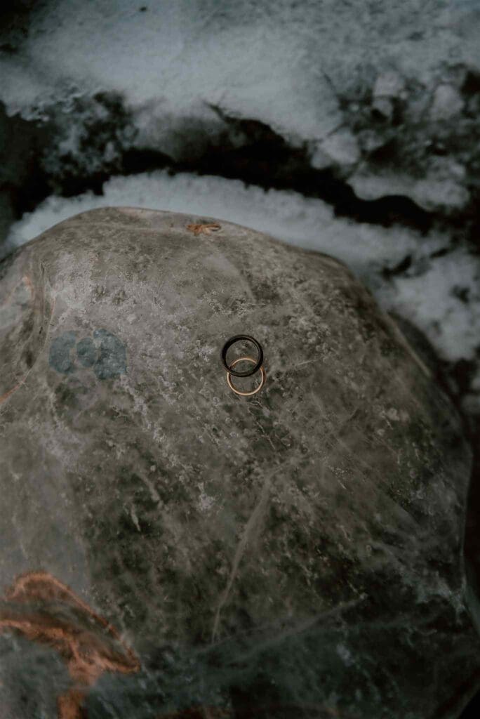 Two male engagement rings sit atop a frozen landscape with ice, snow, and black sands