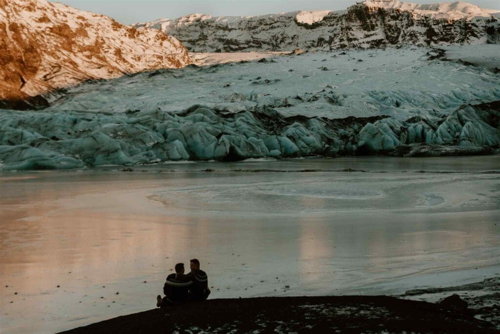 A gay couple sits on black sands overlooking a lagoon at solheimajokull glacier in iceland