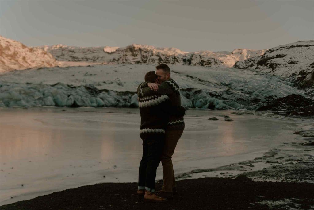 A male couple embraces for engagement photos in a winter Iceland landscape