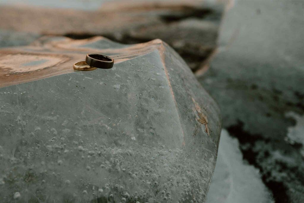 A black and a gold engagement ring for men sit atop an iceberg at a glacier lagoon in iceland