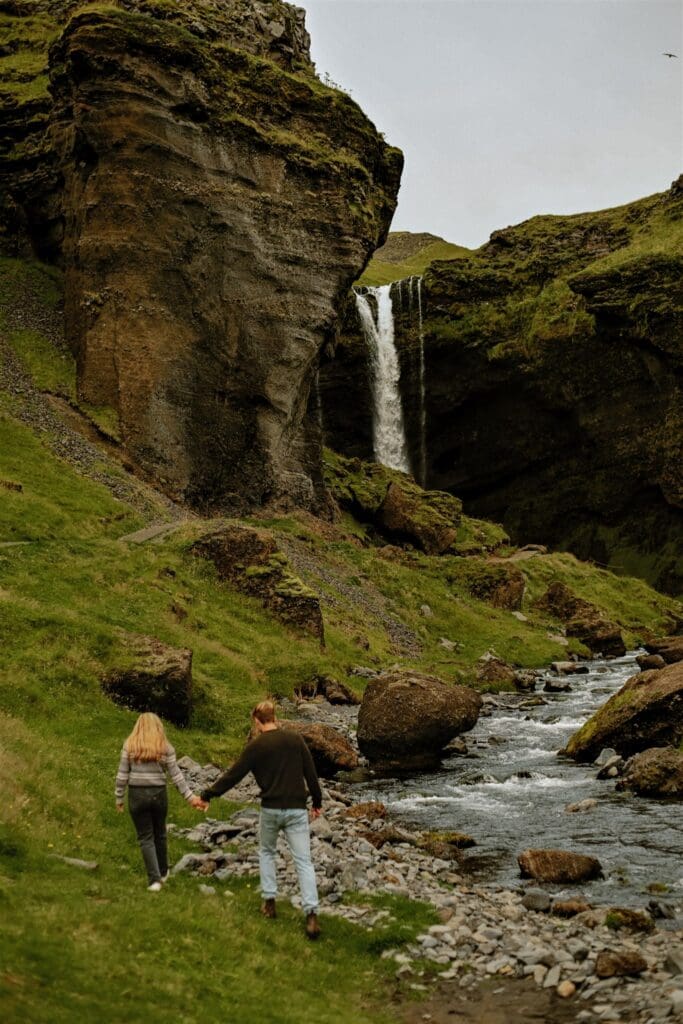 Playful couple holding hands and walking toward a waterfall in Iceland