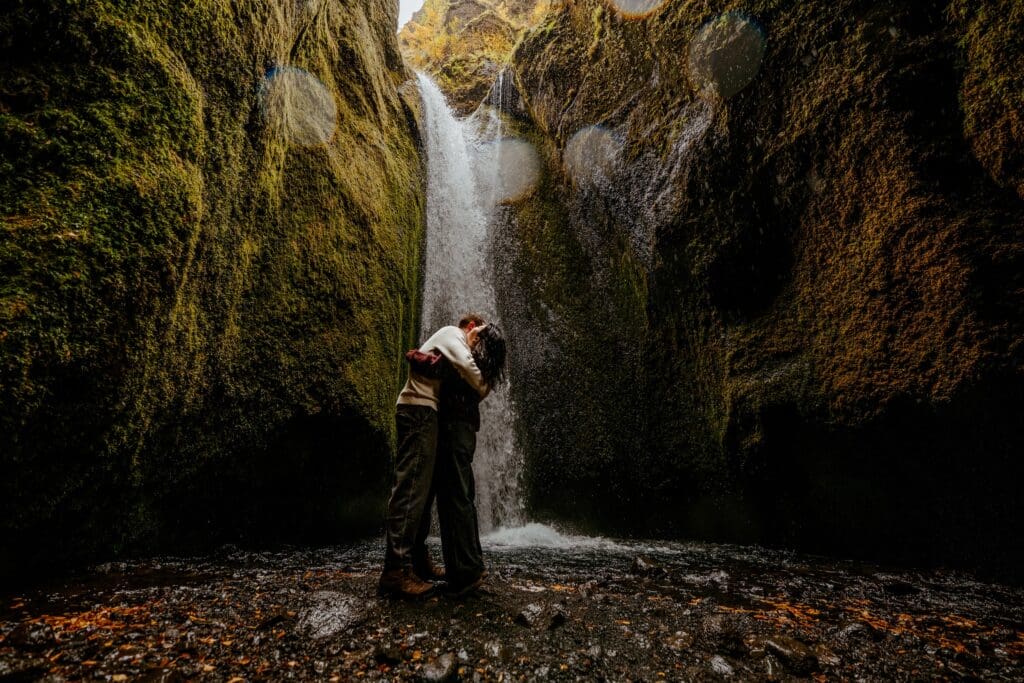 Proposal moment near a waterfall inside a canyon in Iceland with autumn foliage on the wet ground