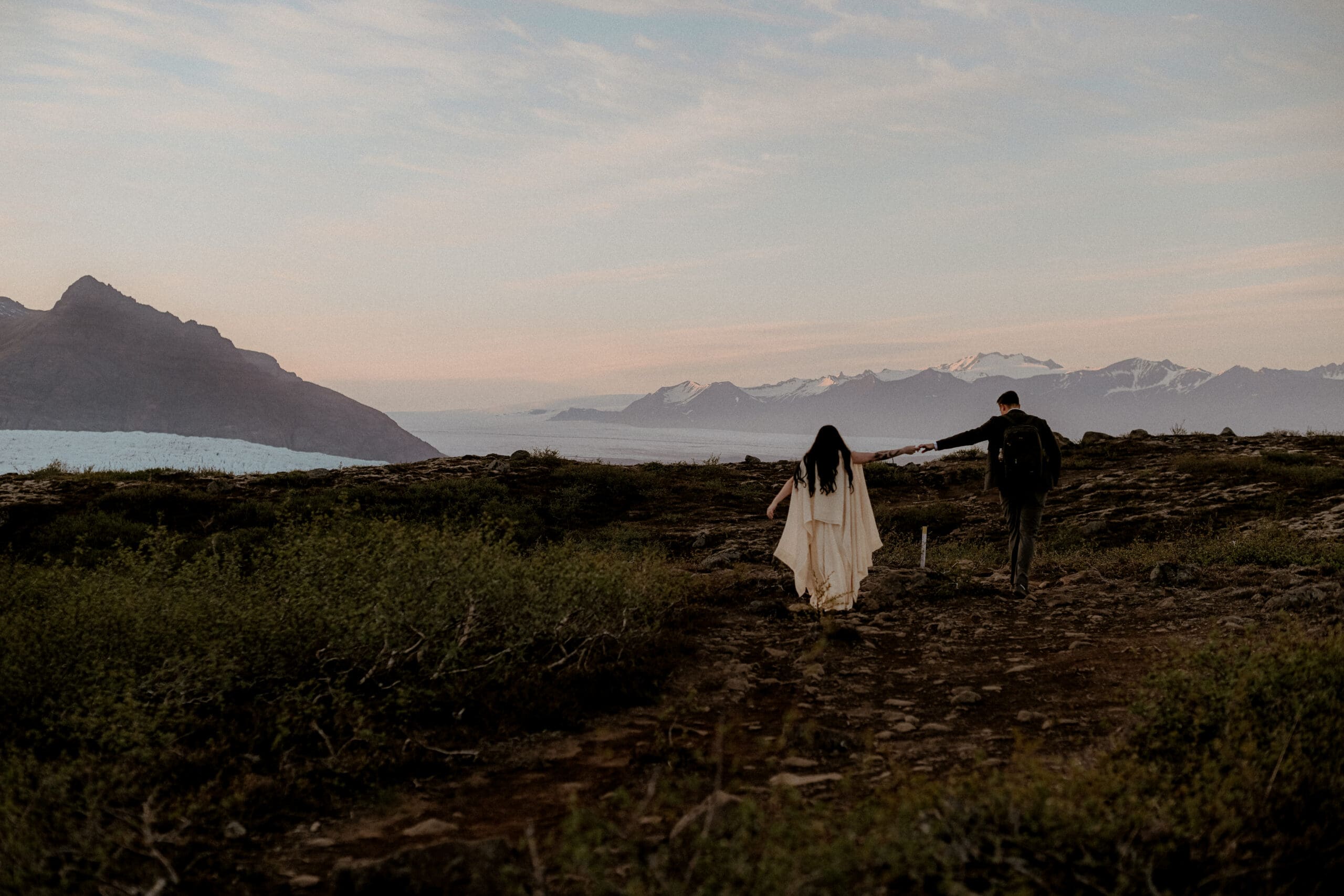 Elopement couple holding hands at golden hour in Iceland with mountains and glaciers in the background