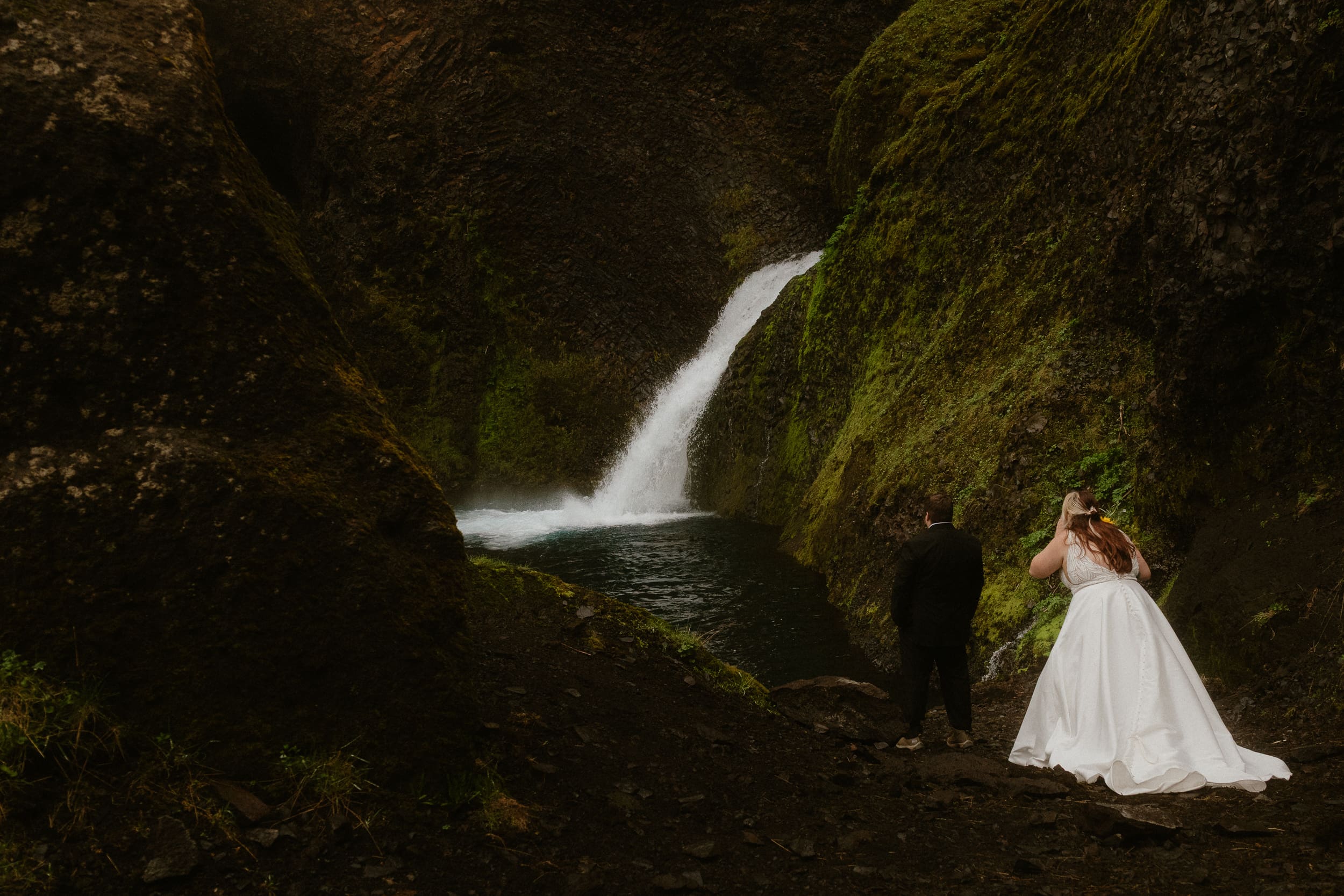 Bride walking toward her groom for a first look at Þakgil canyon in Iceland, with a waterfall in the background, June elopement